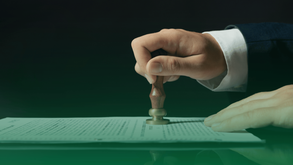 Mão carimbando documento oficial sobre uma mesa, simbolizando aprovação jurídica ou validação contratual.