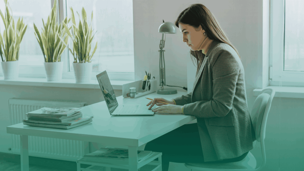Mulher em um escritório bem iluminado, fazendo a checagem de antecedentes através de um notebook.