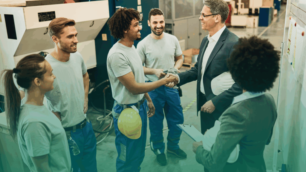 Feliz gerente corporativo apertando as mãos com trabalhador após reunião de equipe em uma fábrica.