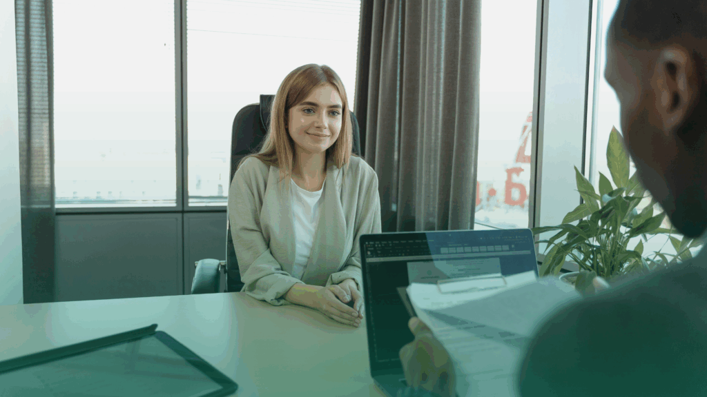 Entrevista de emprego com recrutador verificando currículo enquanto candidata aguarda avaliação, ilustrando a importância da verificação de dados profissionais.
