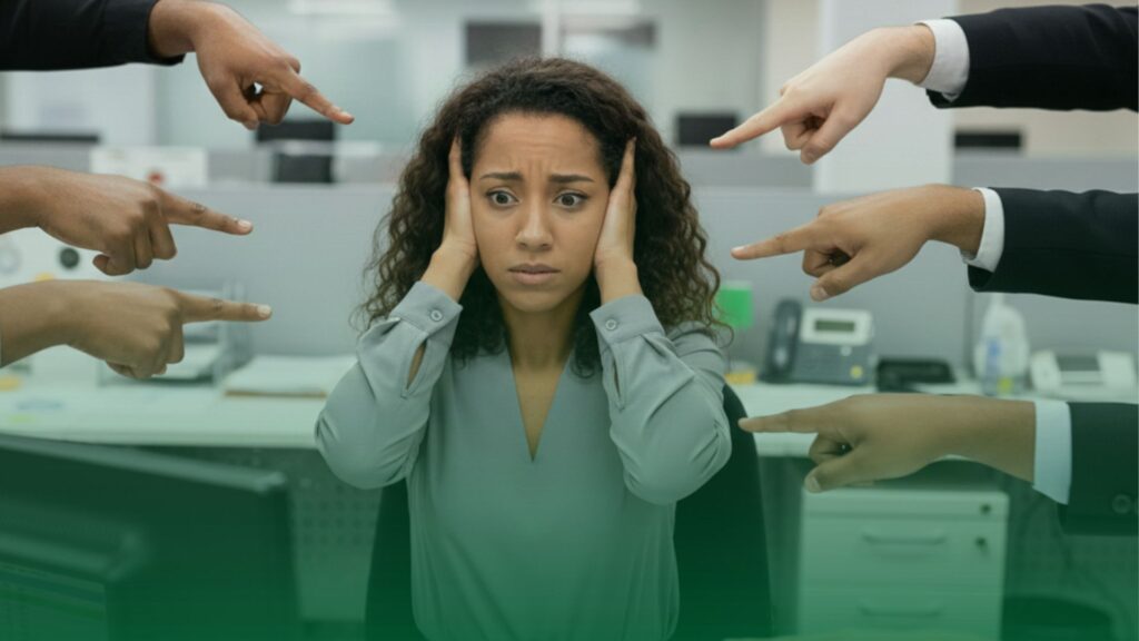 Mulher em escritório expressando estresse e pressão no trabalho, com mãos ao redor apontando para ela, ilustrando riscos psicossociais no ambiente corporativo.
